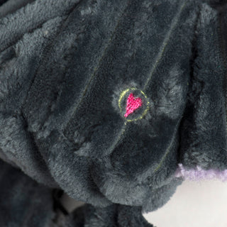 Close-up of another embroidered pink heart with yellow outline on the plush grey body of Baxter Bat.