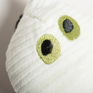 Top-down close-up of white ghost Wee Huggls® Ball with big embroidered green eyes peeking out of mummy-like wrap.
