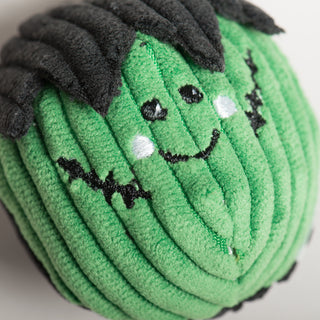 Top-down close-up of green Frankenstein Wee Huggles® Ball with stitched smile and soft black hair.