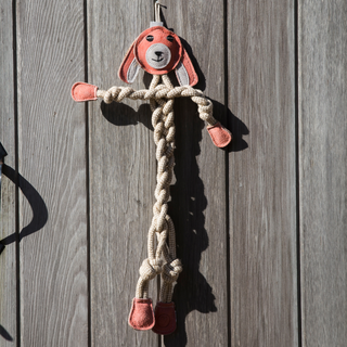 Pink bunny rope dog toy with a pink leather face, white leather hair, pink leather hands and feet, with a rope body, arms, and legs hanging on wall.