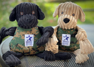 Black and Yellow Lab WCC plush dog toys sitting side by side on a table outside.