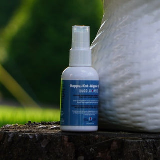 Catnip spray for cats: in a white spray-bottle, with a blue sticker describing the product sitting on tree stump.