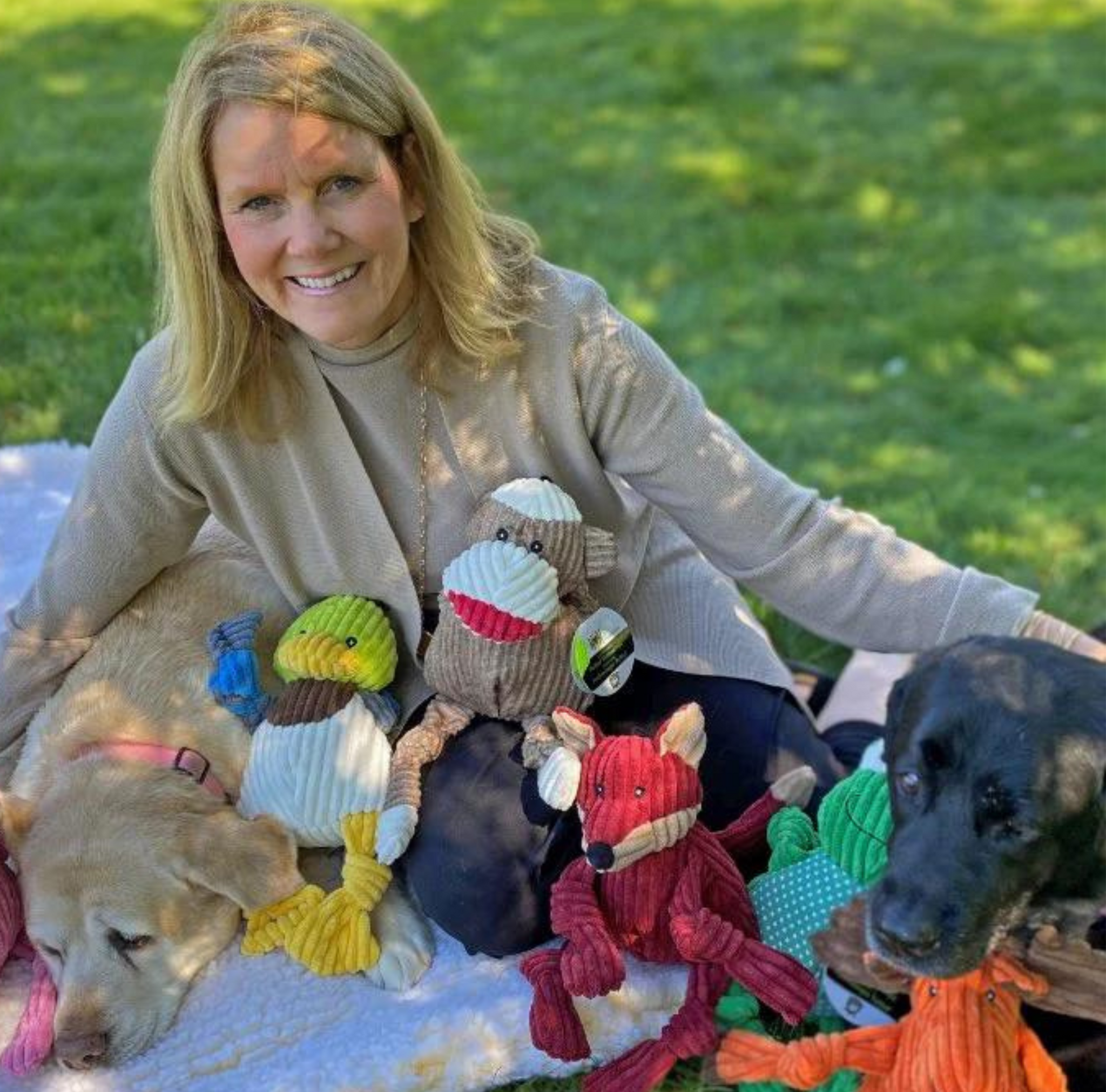 Julie Krauss, Managing Partner & Co-Founder, posed with Knottie® plush toys, and two dogs yellow lab Bridget and black lab Scout