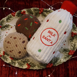 Santa Paws' Milk & Cookies plush toy gift set on holly-themed plate with red background