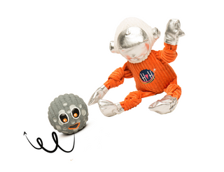 Set of two dog toys: small Astronaut plush dog toy in orange suit with HH logo on chest, white helmet, and silver face dome, gloves, and boots and small grey moon with big orange eyes and smile squeaky ball dog toy. Bouncy line underneath moon squeaky ball indicating that the moon ball bounces.