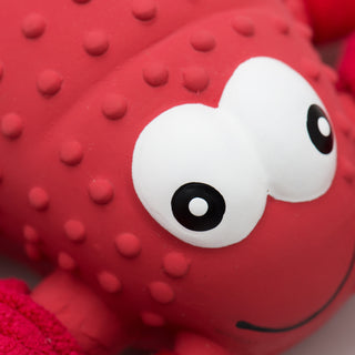 Close up image of lobster shaped durable plush dog toy face: has a textured red shell, black eyes, white pupils, and a wide smile.