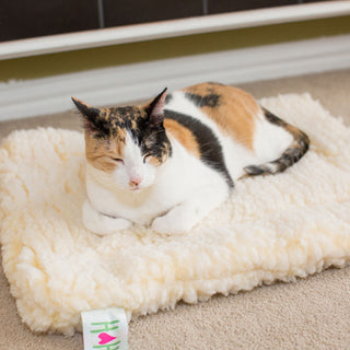 Calico cat laying on xs natural HuggleFleece® mat.