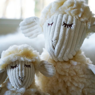 Lifestyle image of set of two lamb shaped plush dog toys in large and small: white fluffy HuggleFleece® body, white limbs, and durable knotted corduroy limbs with squeakers, and brown embroidered eyes and nose.