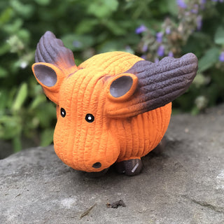 Side view of orange moose squeaky latex ball dog toy with corduroy texture, brown antlers, beard, and feet, and black beady eyes sitting on rock.