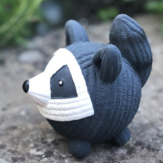Right view of squeaky ball shaped raccoon dog toy: has black and white fur, black tail, white face, black outer-eyes, black nose, and red smile.