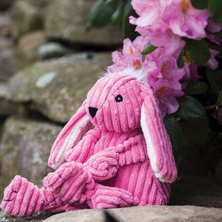 Pink bunny durable plush corduroy dog toy face with white hair and ears sitting on rock.