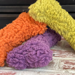 Lifestyle image of all three furry bone plushes on a carpet. The toys are on top of one another.