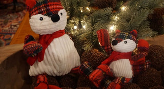 Two foxes made of tartan plaid and white corduroy laying next to evergreen branches and holiday lights