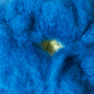 A close-up of a bright blue fuzzy fabric or felt material with a small pale yellow center opening.