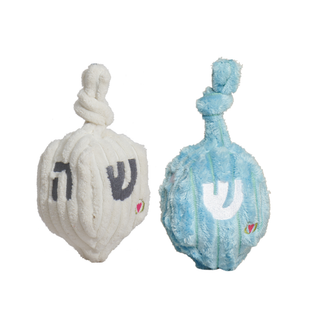 Two plush toy dreidels on a plain white background. One is white with dark gray Hebrew letters and a small pink heart accent.