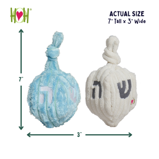 Two plush Hanukkah dreidels shown on a white background with size arrows and text indicating actual size: 7 tall by 3 wide. One dreidel is light blue and one is off-white/cream, both with knotted top handles and Hebrew lettering.