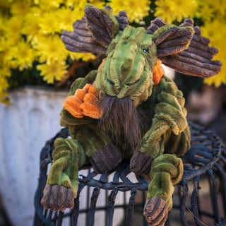 Milo Moose Knottie plush toy posed with yellow flowers in the background, showing corduroy texture and orange scarf.
