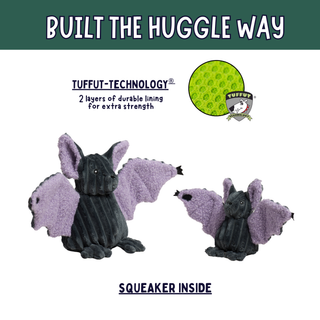 Two plush bat toys on a white background with marketing text. The larger bat is dark charcoal gray with lavender-purple wings, and the smaller bat is the same colorway.