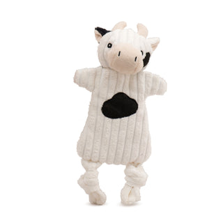 White cow plush dog toy with minimal stuffing, black spots on face and chest, one black ear, beige snout, horns, and inner ears, knotted legs, and black embroidered facial details.