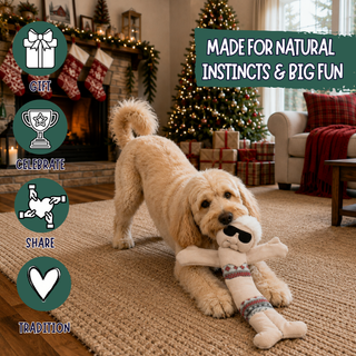 A fluffy cream-colored dog plays with a plush stuffed animal toy in a cozy Christmas-themed living room. The scene includes a fireplace with stockings, wrapped gifts, a decorated Christmas tree, and text overlays reading 'MADE FOR NATURAL INSTINCTS & BIG FUN' plus icons for gift, celebrate, share, and tradition.