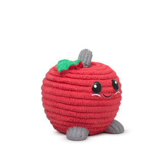 Side view of red apple-shaped latex squeaky ball dog toy in large with red corduroy texture, gray stem and feet, green leaf next to stem, big black eyes, cute black smile, and cute pink cheeks.