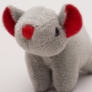 Close up view of mouse shaped, catnip stuffed cat toy face: has gray fur, black eyes, red nose, and red inner-ear.