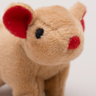 Close up view of mouse shaped, catnip stuffed cat toy face: has light-brown fur, black eyes, red nose, and red inner-ear.