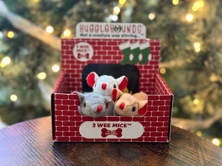 Set of three mice shaped, catnip stuffed cat toys: each mice has black eyes, red inner-ear, and a red nose. There is a white furred mice, a light-brown furred mice, and a gray furred mice. Three mice are sitting in display box packaging designed to look like a classic red brick fireplace with Christmas tree in background.