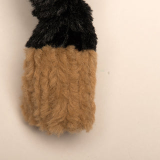 Close up image of dog shaped durable plush dog toy, has black fur, and it's knotted limb with light-brown paw.