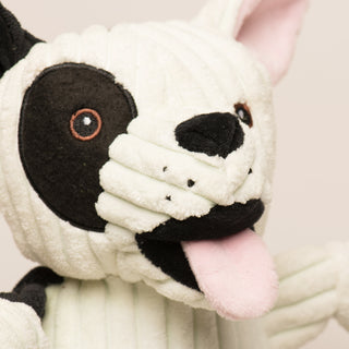 Close up image of a Jonny Justice durable plush corduroy dog toy to show details in face: The dog has black and white fur, right outer-eye is black, has brown eyes, white pupils, plush out black nose, black mouth, pink tongue, and is squeaky.  