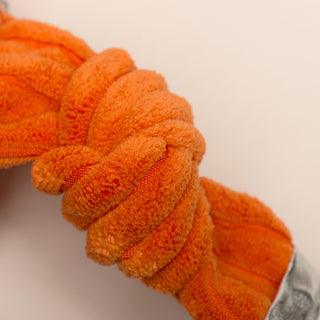 Close-up of an orange knotted rope toy on a neutral background