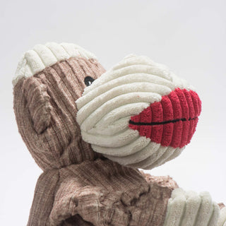 Close up side view to show texture of corduroy fabric. Brown and white sock monkey durable plush corduroy dog toy with knotted limbs, white top of head, face, and big red lips.