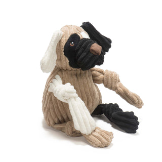 Left view of dog shaped plush dog toy: has brown fur, with white furred right ear, black furred left ear, black fur on right outer-eye, white fur on left outer-eye, black lips, brown nose, white right arm, black left leg, and has knotted limbs.