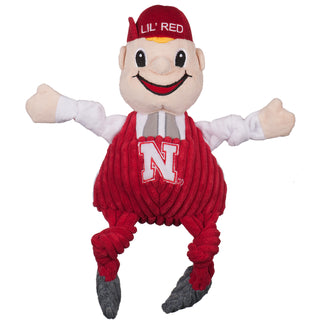 University of Nebraska Lil Red mascot plush dog toy with beige, skin tone face and hands, white long sleeved undershirt, red corduroy overalls with embroidered university logo, grey corduroy shoes, big nose, embroidered eyes and mouth, and red hat with words "LIL' RED" and blond hair poking out underneath hat. Size large.