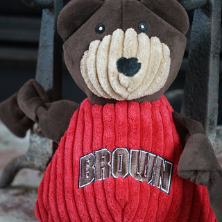 Top half of Brown University Bruno the bear durable plush corduroy dog toy with brown knotted limbs, brown head, tan face, and a red shirt with the University logo on chest.