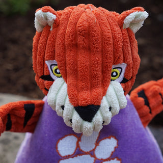 Close up of Clemson University the Tiger durable plush corduroy dog toy face with orange fur, white inner-ear, white outer-eye, yellow eyes with white pupils, black nose, and a white mouth. 
