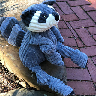 Left side view of raccoon shaped plush dog toy sitting on a stone slab looking up.  