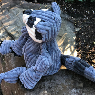 Right side view of raccoon shaped plush dog toy sitting on a stone slab. 