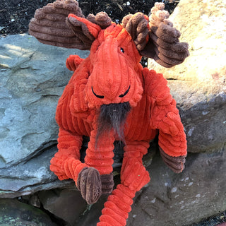 Orange moose durable plush corduroy dog toys in large and small with knotted limbs, brown antlers, inner ears, and hooves, hairy brown beard tuft, and black embroidered eyes and nostrils sitting on rock.