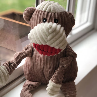 Brown and white sock monkey durable plush corduroy dog toy's sitting on window sill.