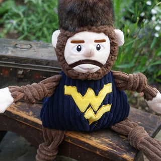 West Virginia University Mountaineer mascot durable plush corduroy dog toy with knotted limbs, brown sleeves, legs, beard and hair, brown fur hat, and navy shirt with West Virginia University logo on the front.