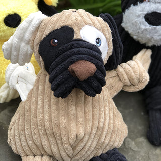 Dog shaped plush dog toy: has brown fur, with white furred right ear, black furred left ear, black fur on right outer-eye, white fur on left outer-eye, black lips, brown nose, white right arm, black left leg, and has knotted limbs.